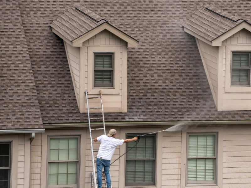 man-standing-on-ladder-pressure-washing-top-floor-siding-and-roof2 (1)